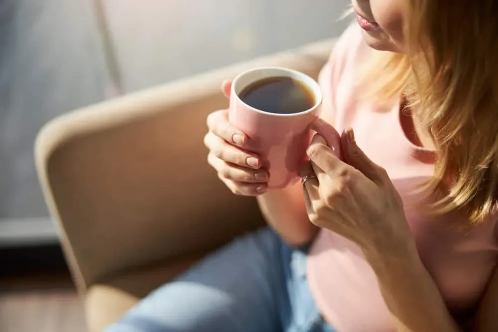 Bàn tay đang đặt lên tách cà phê nóng, thể hiện sự thư giãn và cách phòng tránh say cà phê