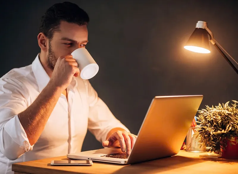 Hình ảnh ly cà phê đã uống gần hết đặt cạnh giường ngủ với đồng hồ báo thức