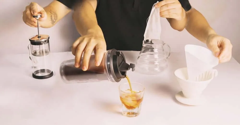 Hình ảnh một người đang thực hiện các bước pha cà phê viên nén thủ công với nước nóng và cốc, minh họa chi tiết quy trình.