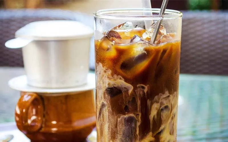 Một ly cà phê sữa đá được trang trí đẹp mắt đặt bên cạnh các hạt cà phê nguyên chất